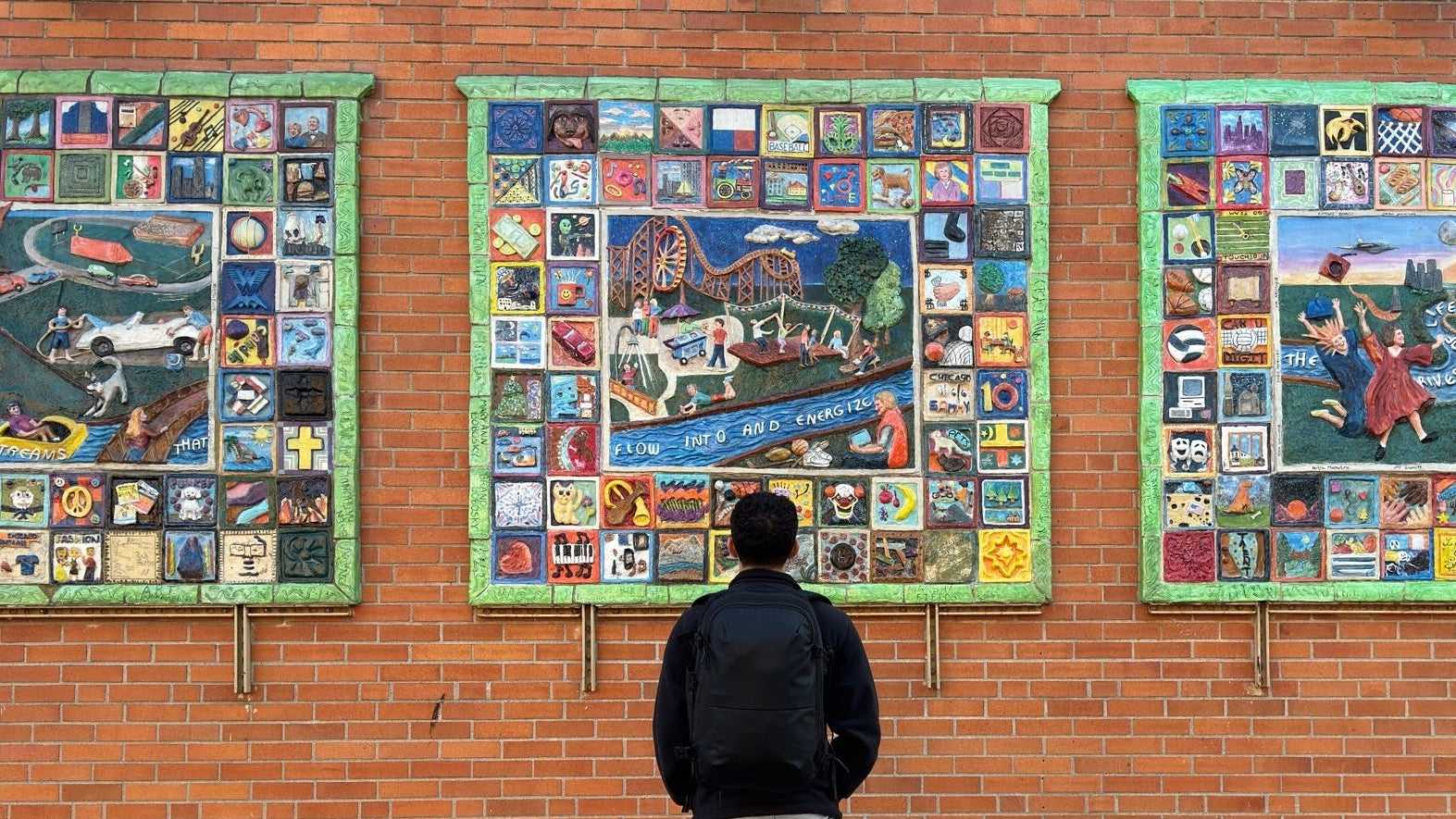 Person standing in front of a brick wall with three colorful murals.